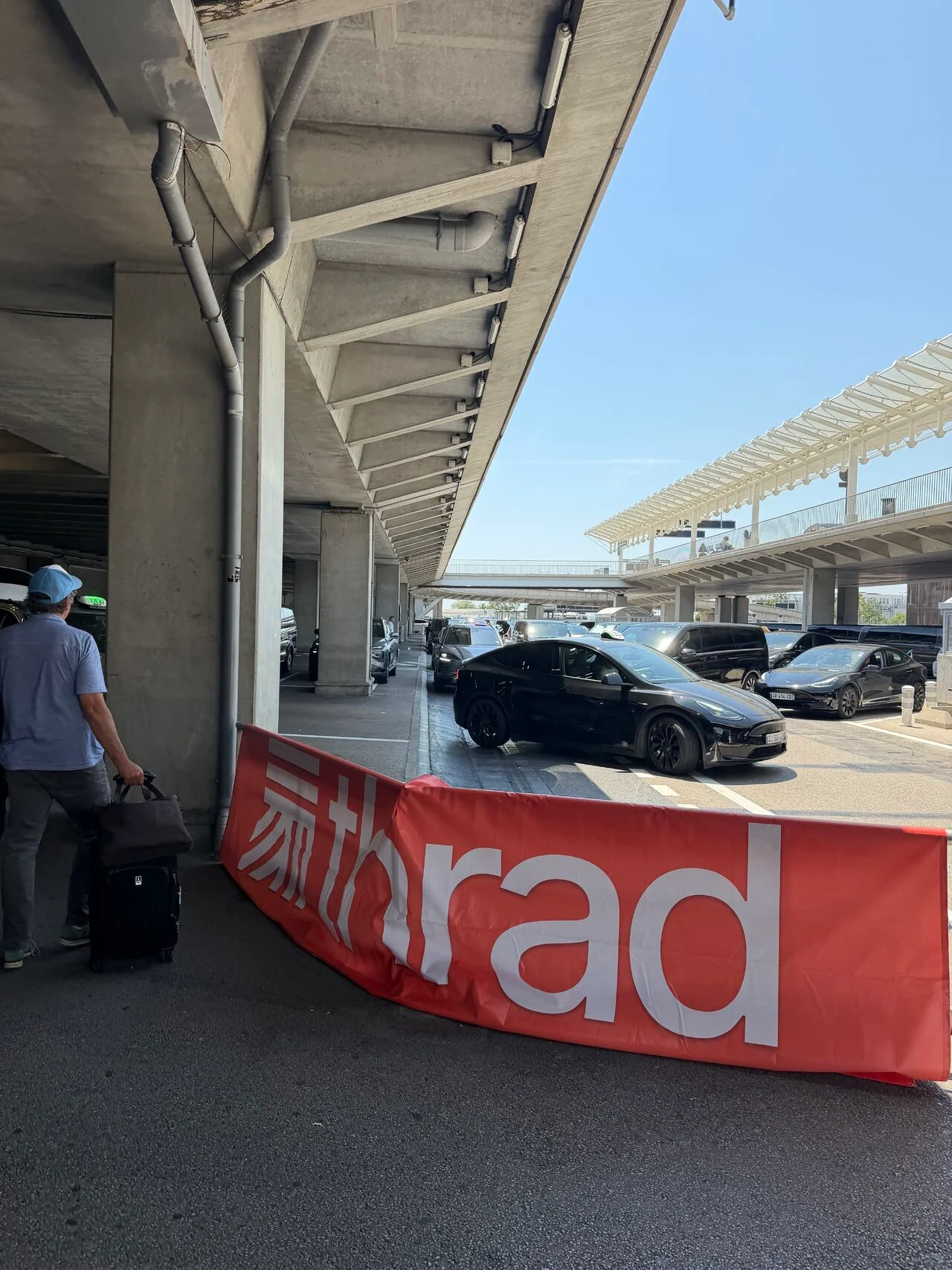 A Thrad banner at the airport taxi rank, with arriving travellers and cars